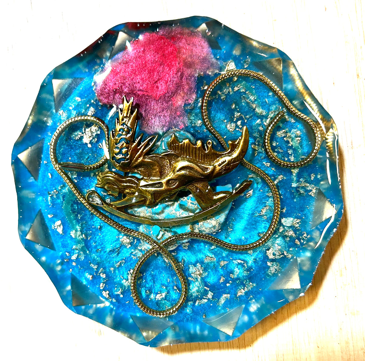 Golden Dragon resin paperweight — overhead view showing gold dragon figurine, swirling gold chain, pink floral puff and silver leaf flakes in electric blue faceted diamond-edge resin disc