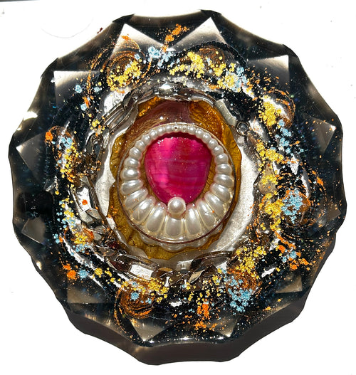 Black Pearl Abyss resin paperweight — overhead view of round disc with faceted scalloped edges showing deep pink magenta teardrop stone in pearl-edged oyster brooch setting with silver serpent chain coiling around it in deep black resin with gold leaf and orange teal glitter