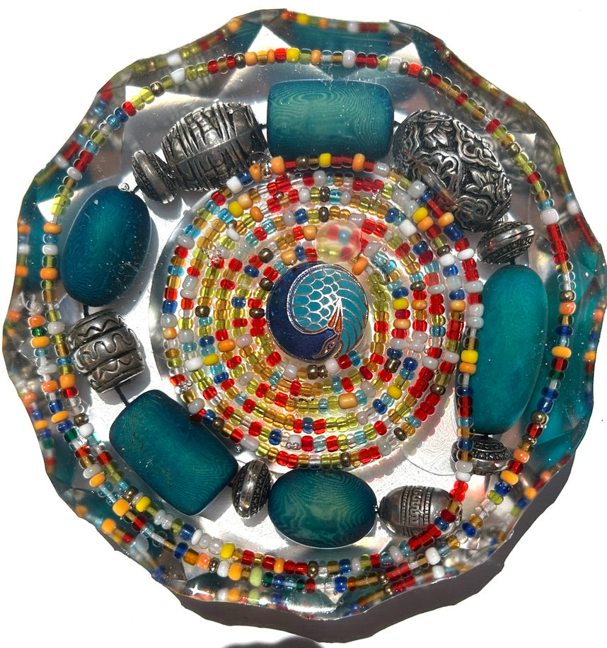 Teal cosmos bead paperweight with cloisonné center, matte teal glass beads, silver accents, and multicolor seed bead rings set in a faceted clear resin dome