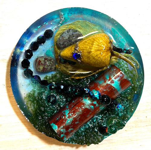 Enchanted Garden resin paperweight — overhead view showing resinized real rose with wire-wrapped blue cabochon, red jasper slab, tumbled stones and black faceted beads in teal green smooth-edge resin disc
