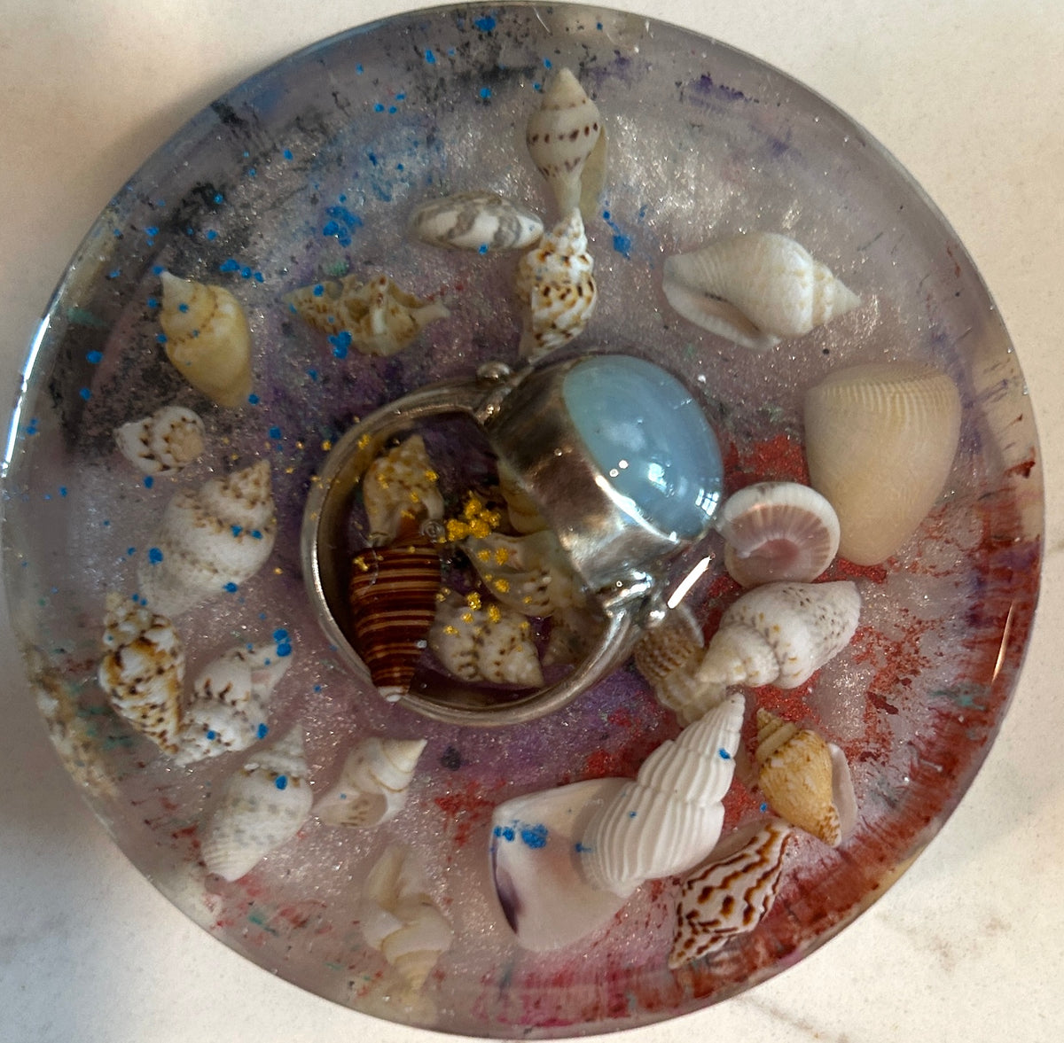 Round resin paperweight with white spiral seashells, silver larimar ring, wood coral, and violet-blue shimmer field