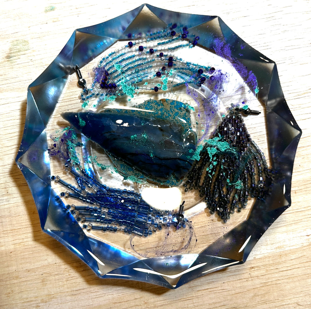 Kyanite Storm resin paperweight — overhead view showing blue kyanite blade crystal, cobalt and gunmetal bead fringe, teal glitter shimmer and purple accents in faceted diamond-edge resin disc