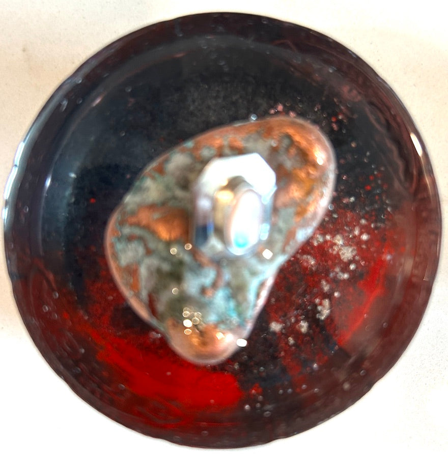 Round resin paperweight with deep black and crimson swirl field, silver glitter, and luminous abalone shell center