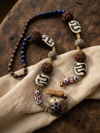 Handcrafted necklace with dzi beads, rudraksha, lapis, chevron trade beads and Kashmiri locket pendant on linen