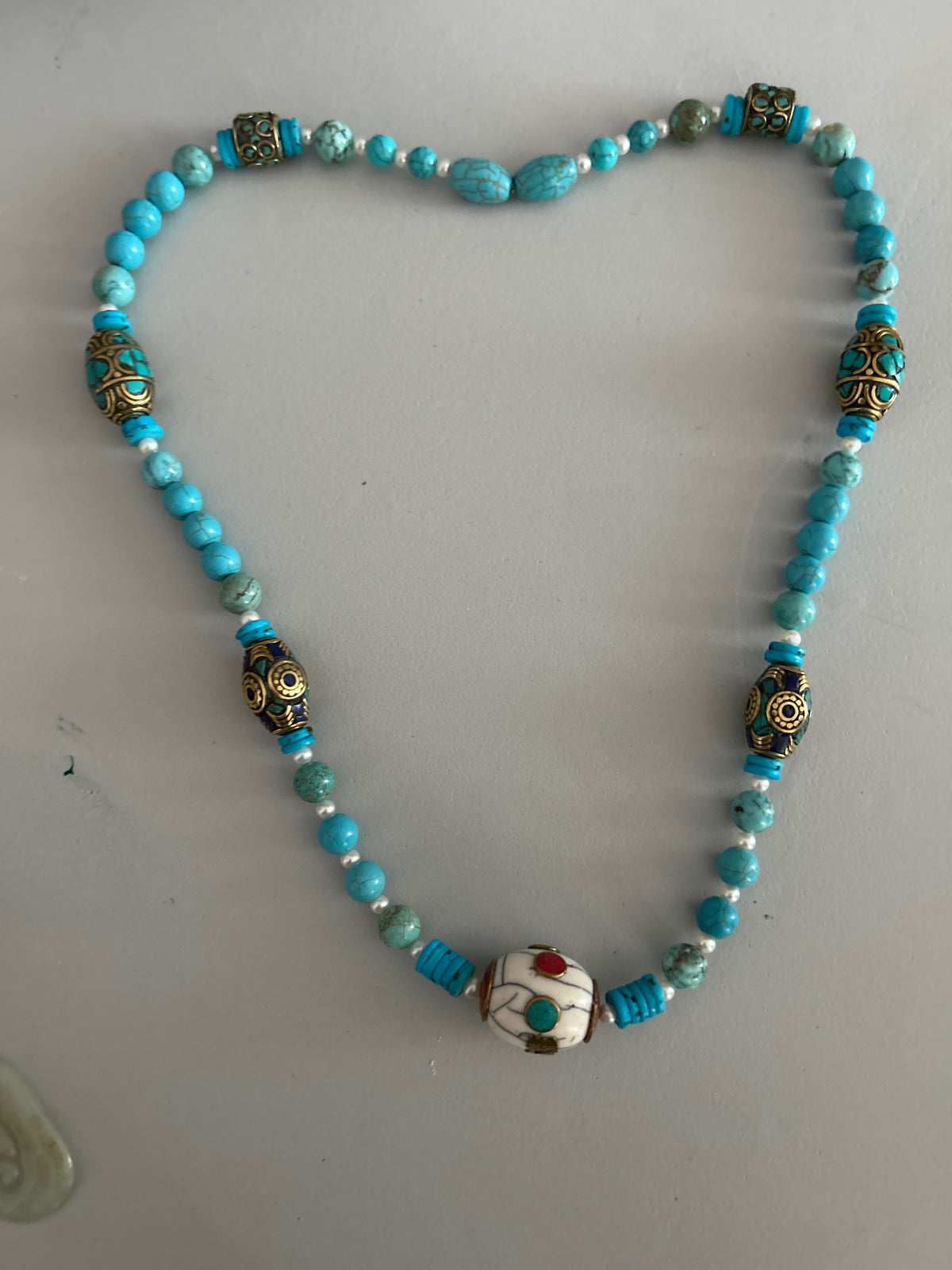 Tibetan turquoise and pearl necklace with brass inlay beads and white focal bead on white background