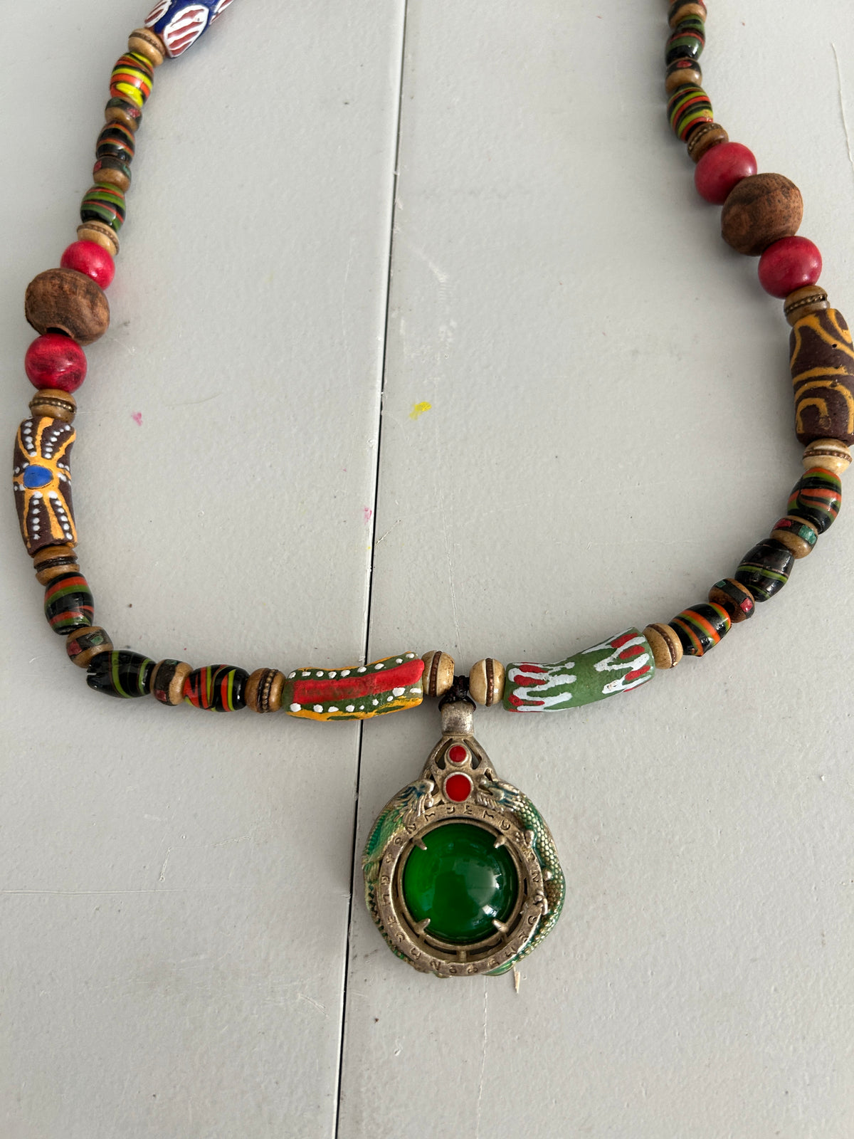 African trade bead necklace with Tibetan silver dragon pendant set with emerald green jade cabochon on white background