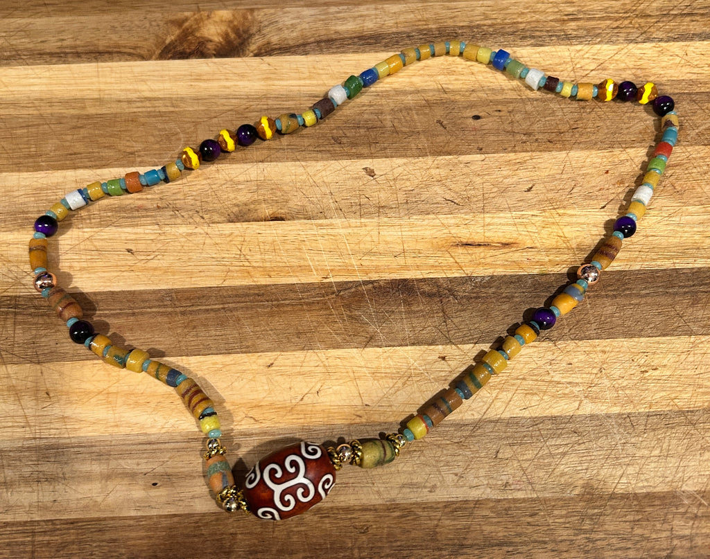 Multicolor African heishi beaded necklace with amethyst and agate dzi centerpiece on wood