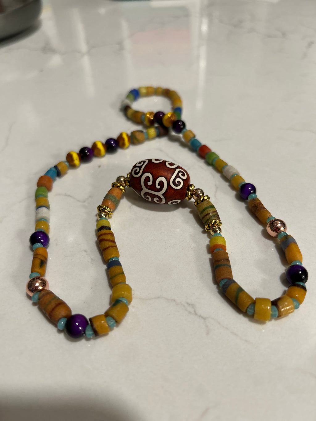 Multicolor African heishi beaded necklace with amethyst and agate dzi centerpiece on marble