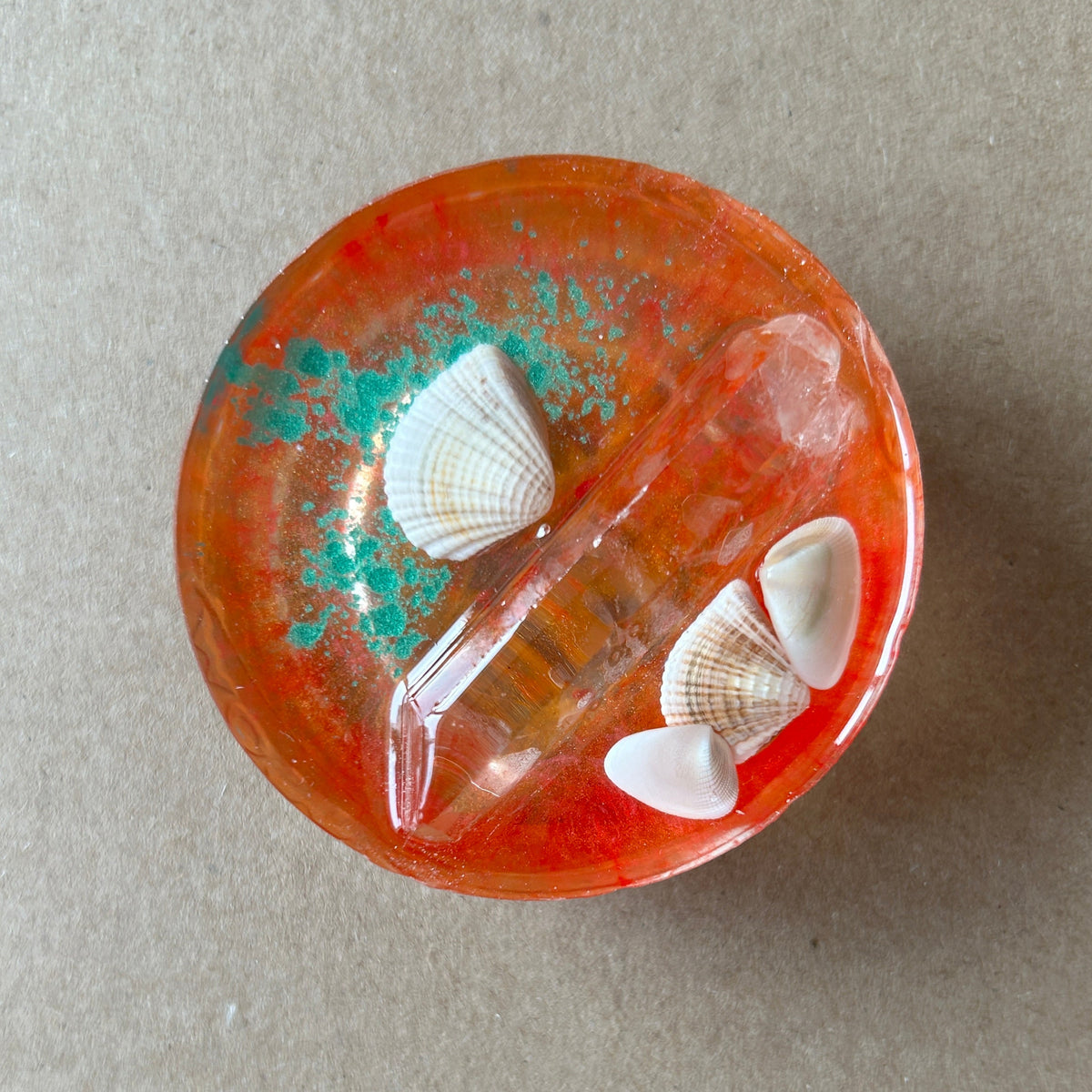 Orange resin paperweight with pale seashells, turquoise-colored flecks, a clear crystal-like point and a pale pink accent.