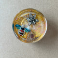 Golden resin paperweight featuring turquoise-winged bee, sparkling silver-toned flower and sunburst accent.