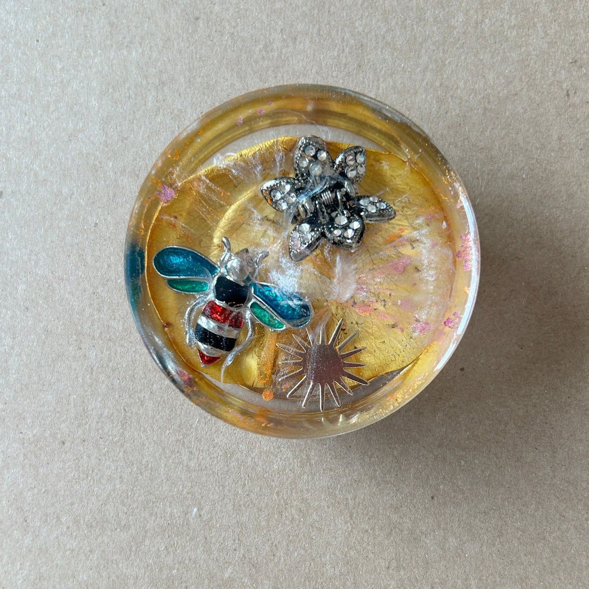 Golden resin paperweight featuring turquoise-winged bee, sparkling silver-toned flower and sunburst accent.