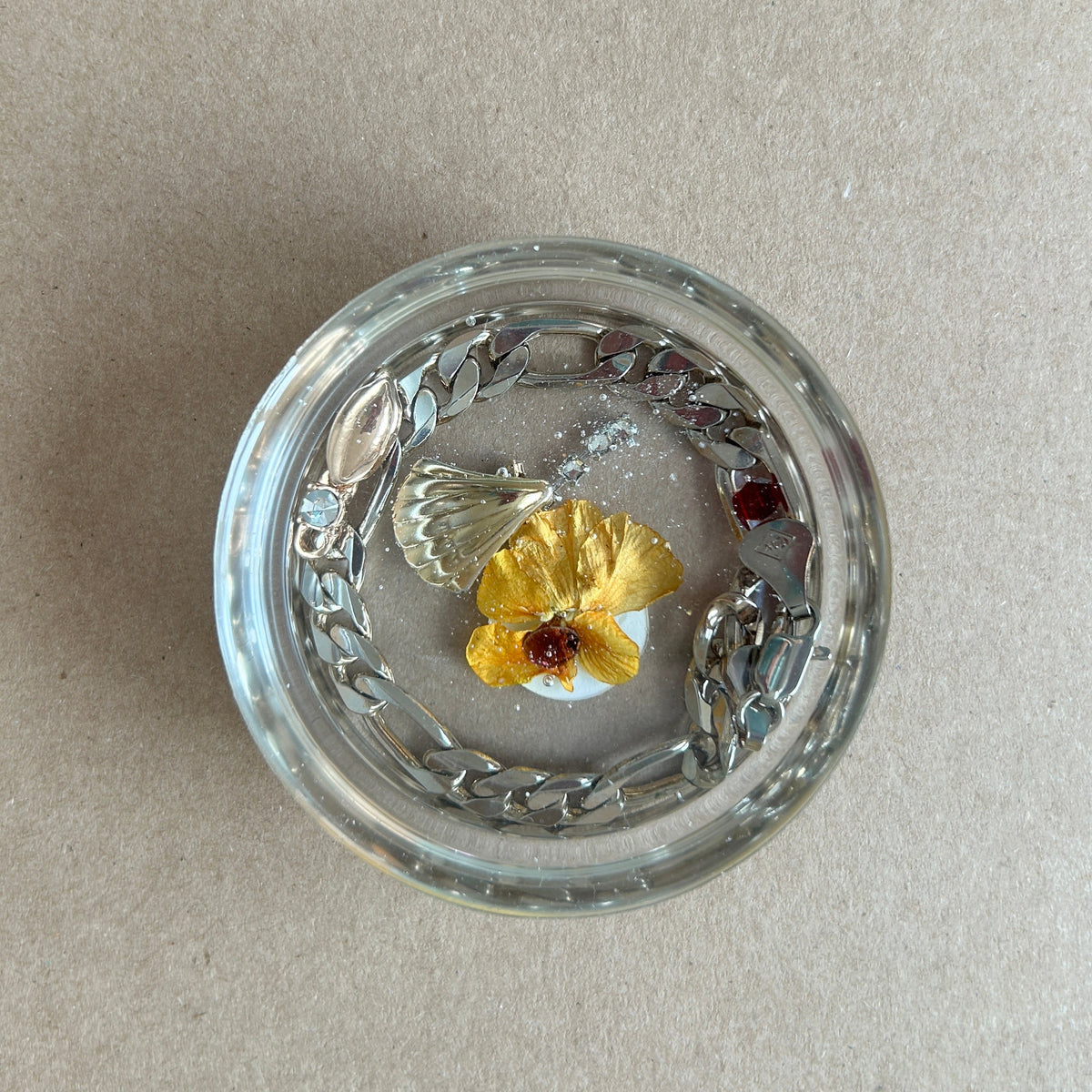 Clear round resin paperweight with yellow flower, silver-toned chain border and fan-shaped metallic charm.