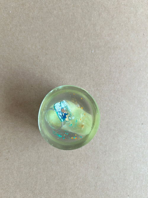 Pale green paperweight with a blue-and-white floral accent and scattered reflective flecks
