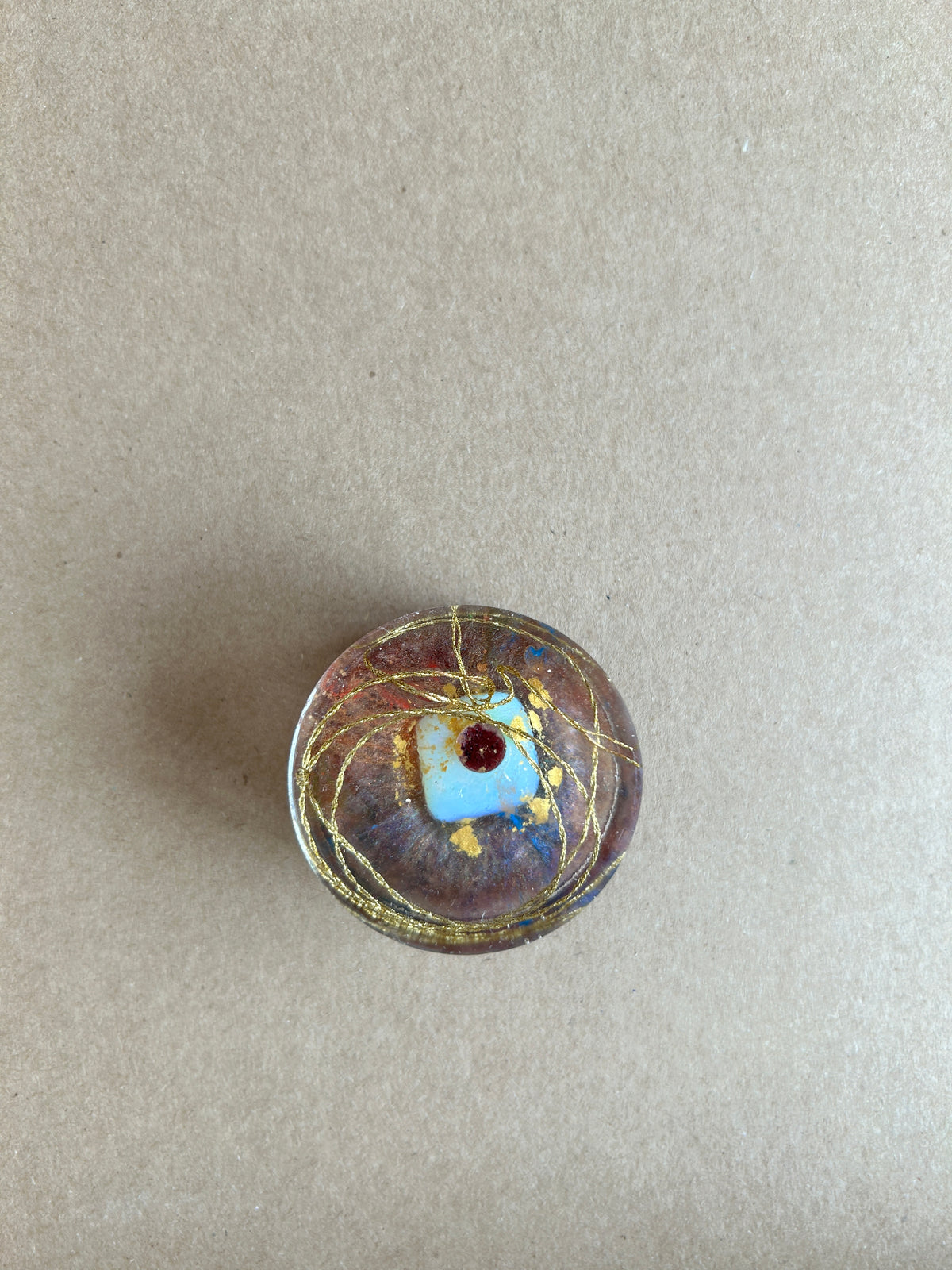 Looping gold-colored strands around a pale blue square and dark red accent in clear resin