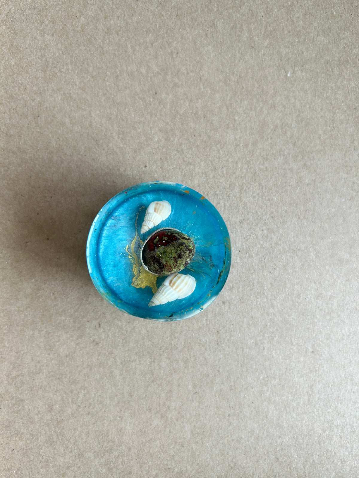 Bright blue paperweight with two pale spiral shells and a dark textured oval centerpiece