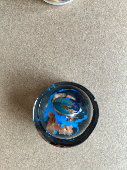 Oval blue patterned ornament and copper-colored textures against dark resin with vivid blue accents