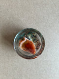 Warm amber-and-cream banded centerpiece over dark green and metallic textured flecks in clear resin