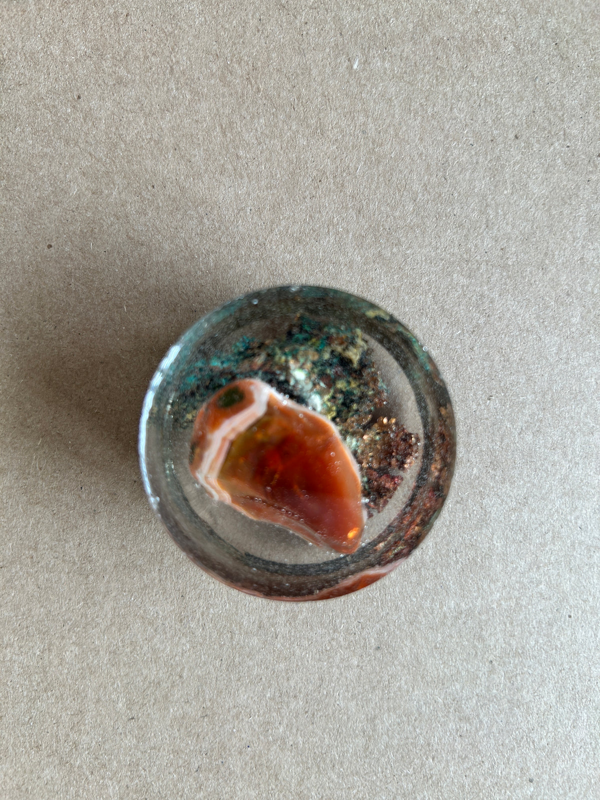 Warm amber-and-cream banded centerpiece over dark green and metallic textured flecks in clear resin