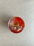 Orange-red resin paperweight with a textured copper-colored form and rectangular gold-toned detail