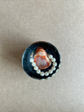 Orange-and-cream banded crystalline centerpiece with curved pearly white beads against dark resin