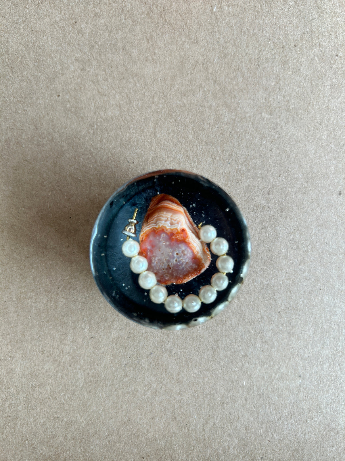 Orange-and-cream banded crystalline centerpiece with curved pearly white beads against dark resin