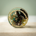 Gilded Keepsake paperweight with cream bead border, miniature perfume bottle and golden bow on an ivory background