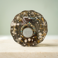 Moonlit Regalia paperweight with an ornate circular centerpiece, white pearl-like beads and golden flakes on a light background
