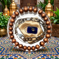 Evil Eye Talisman resin paperweight on Moroccan riad courtyard background with intricate blue and gold mosaic zellige tiles, ornate golden lanterns and lush greenery