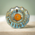 Amber Bloom paperweight with orange floral centerpiece and ornate gold-toned charms on a light ivory-and-sage background